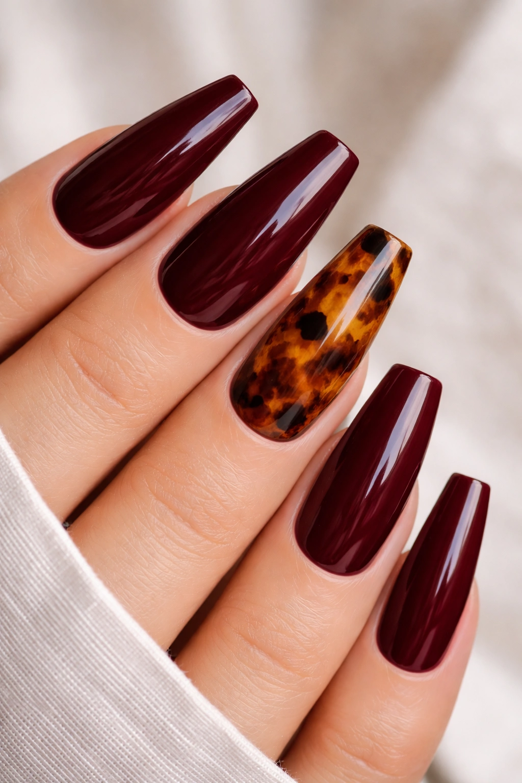 Tortoiseshell accent nails paired with solid burgundy ballerina nails.