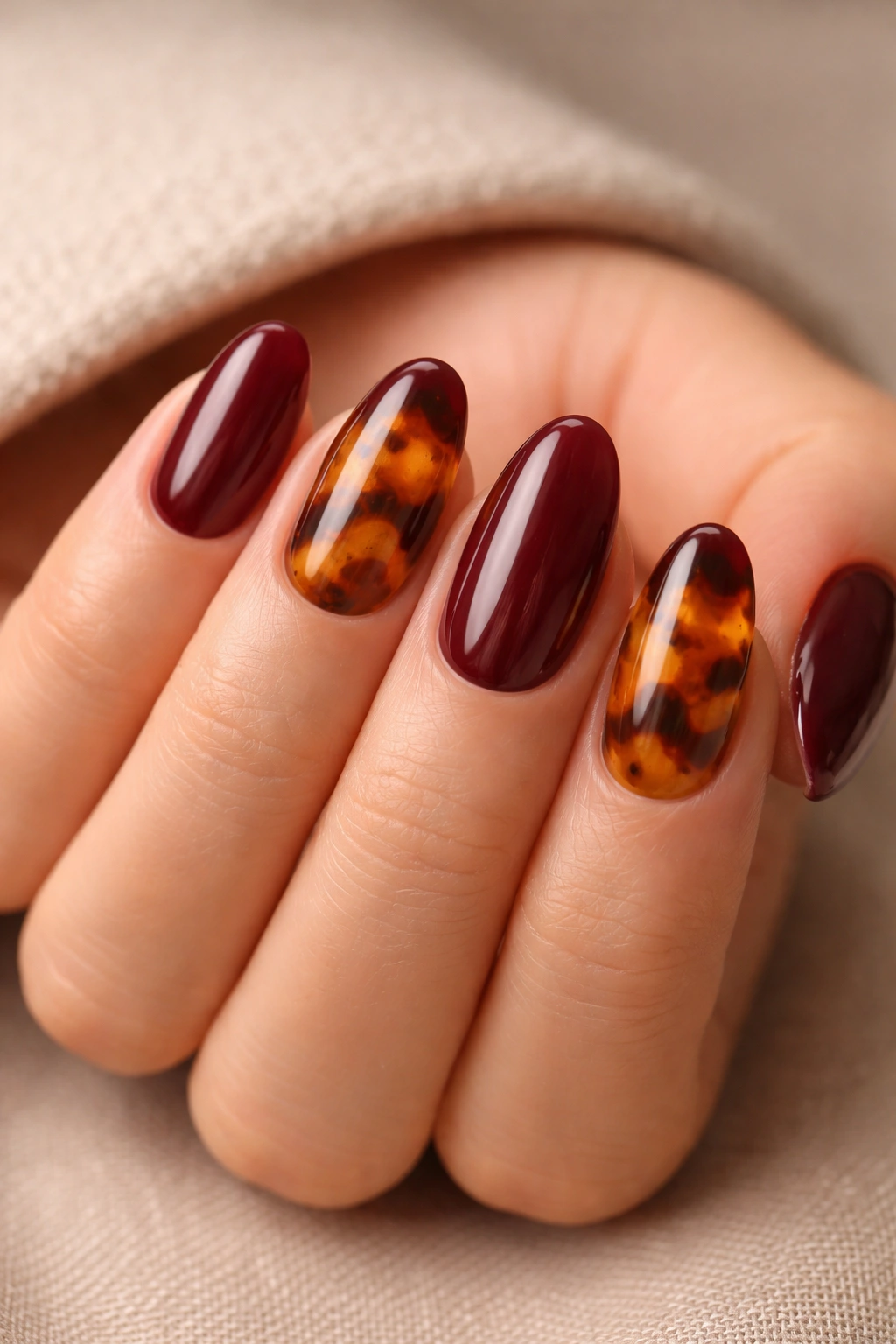 Close-up of short almond nails alternating tortoiseshell and maroon finishes
