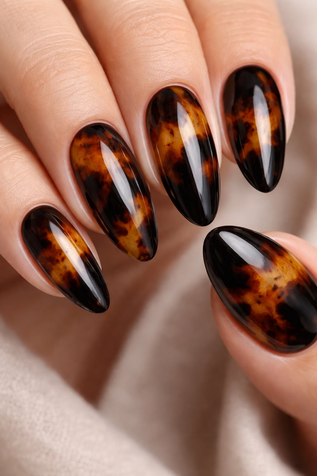Close-up of black tortoiseshell nails with amber and brown swirls on a sheer base.
