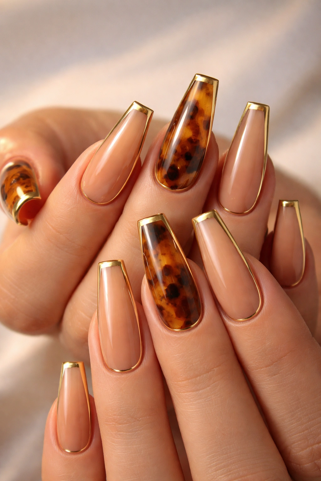 Close-up of tortoiseshell nails with gold framed edges on ballerina-shaped nails