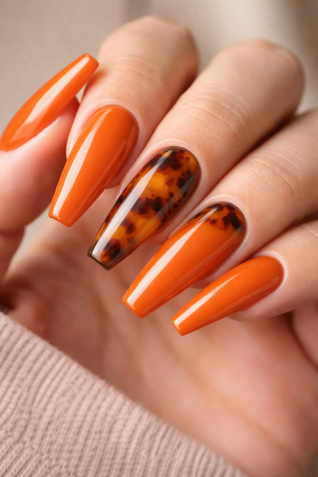 Nail close-up showing tortoiseshell accent nails on a pumpkin-orange manicure.
