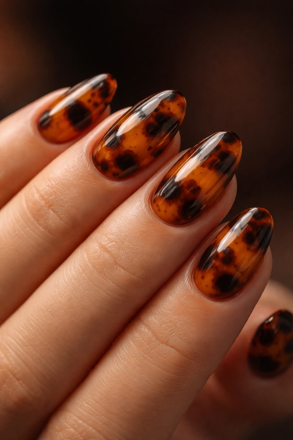 Close-up of tortoiseshell short almond nails with amber and brown patterns.