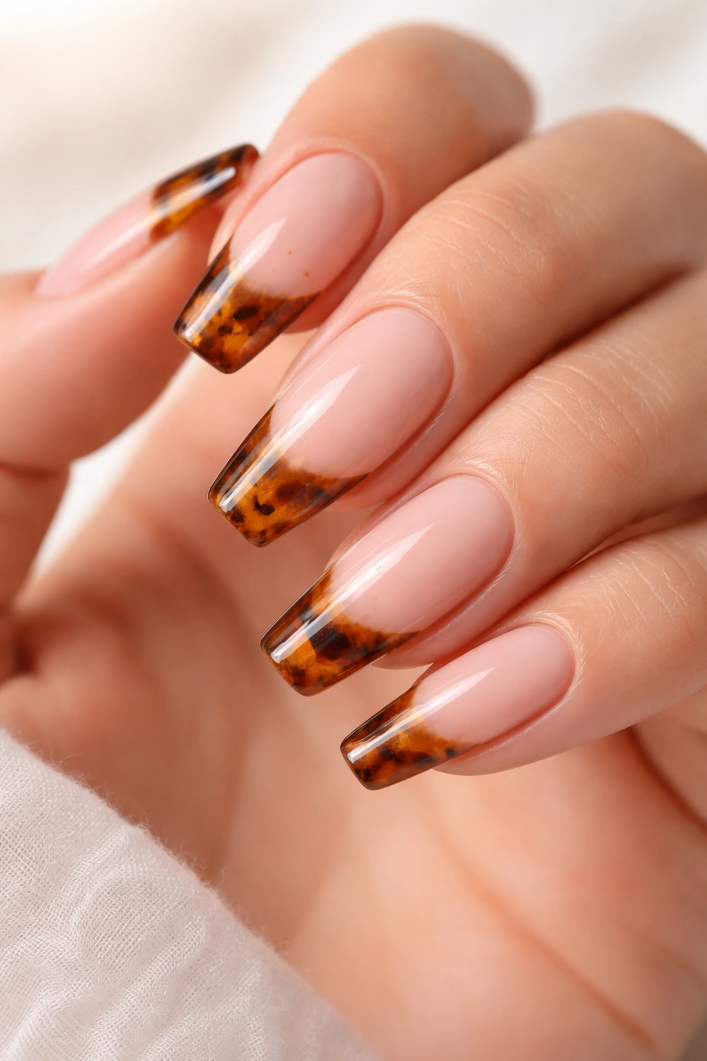 Close-up of tortoiseshell tip ballerina nails on a nude base.