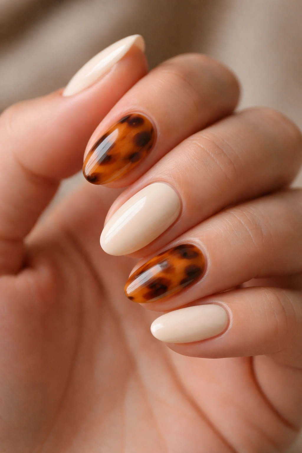 Close-up of a hand with short almond nails featuring a tortoiseshell and vanilla combo design
