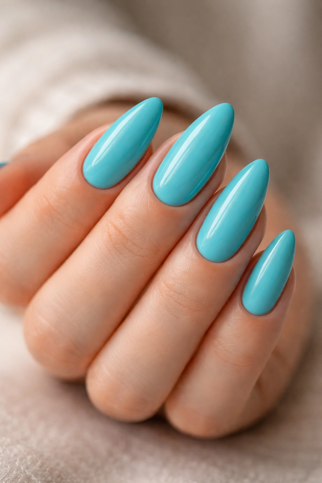 Close-up of turquoise almond nails with glossy turquoise polish