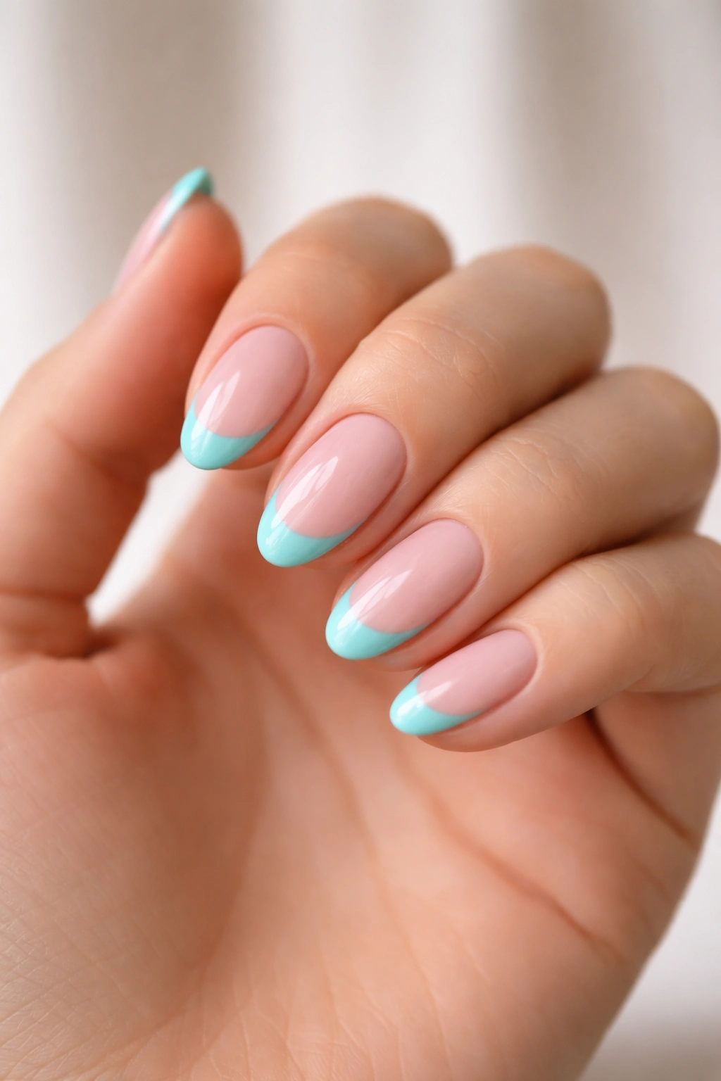 Close-up of short almond nails with turquoise French tips on sheer pink base