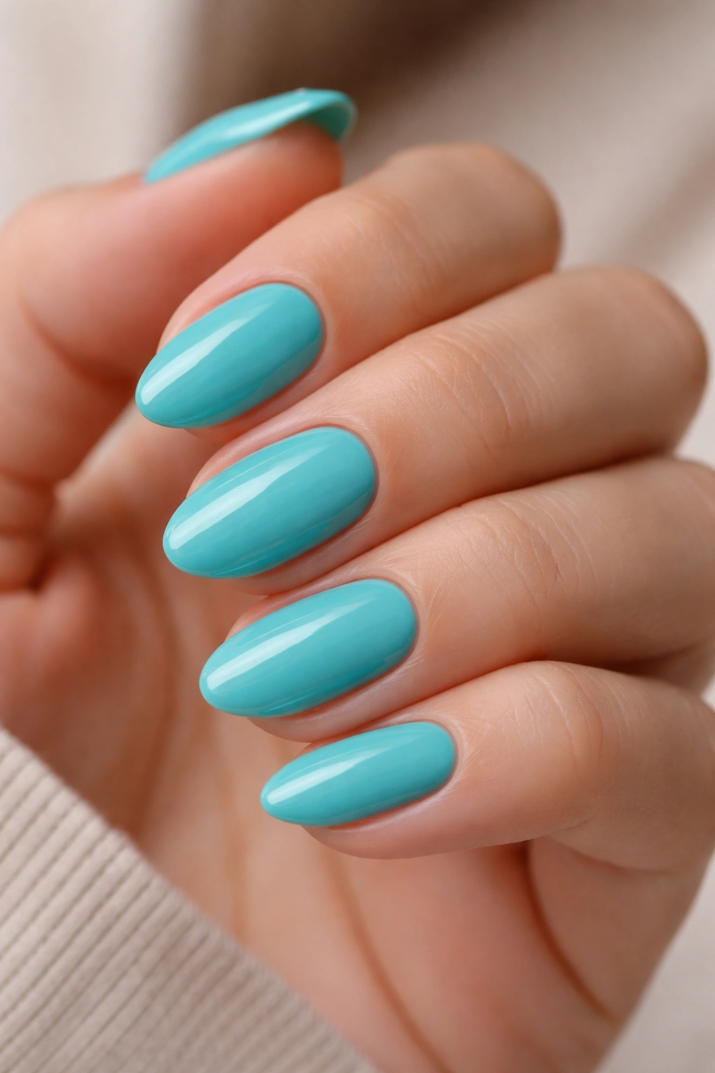 Close-up of short almond turquoise nails with glossy finish on a neutral background