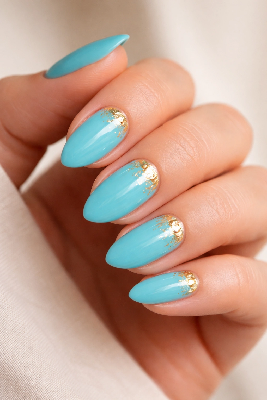 Close-up of turquoise nails with small gold foil accents on short almond nails