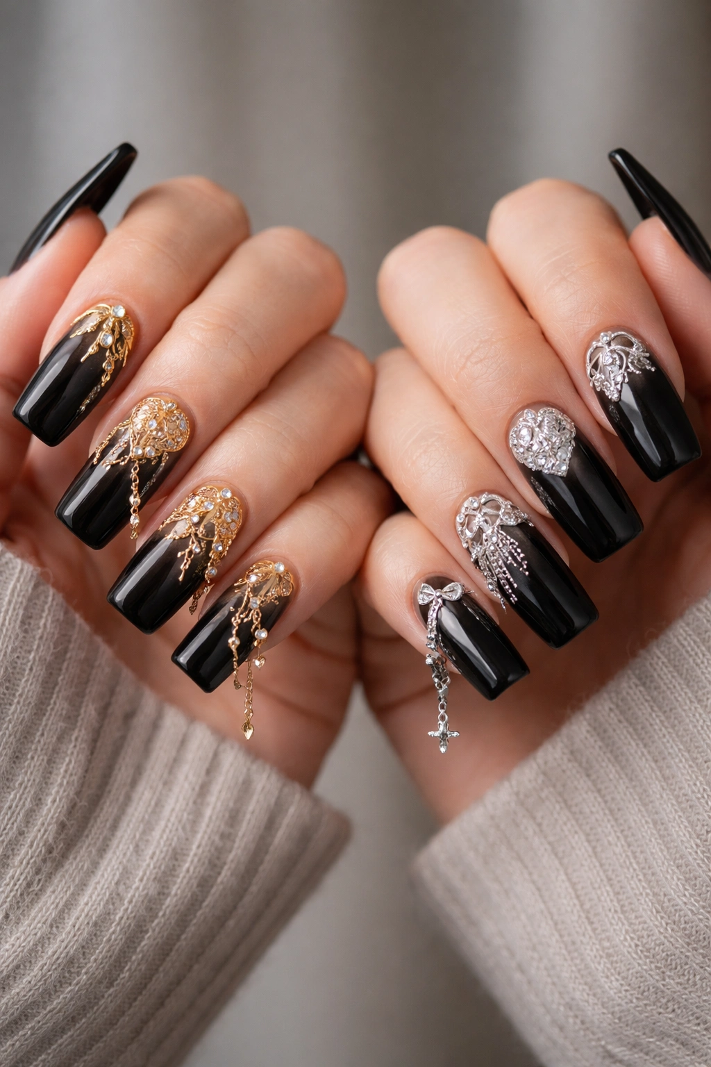 Close-up of hands with two-tone gold and silver charm nails on black ombre base