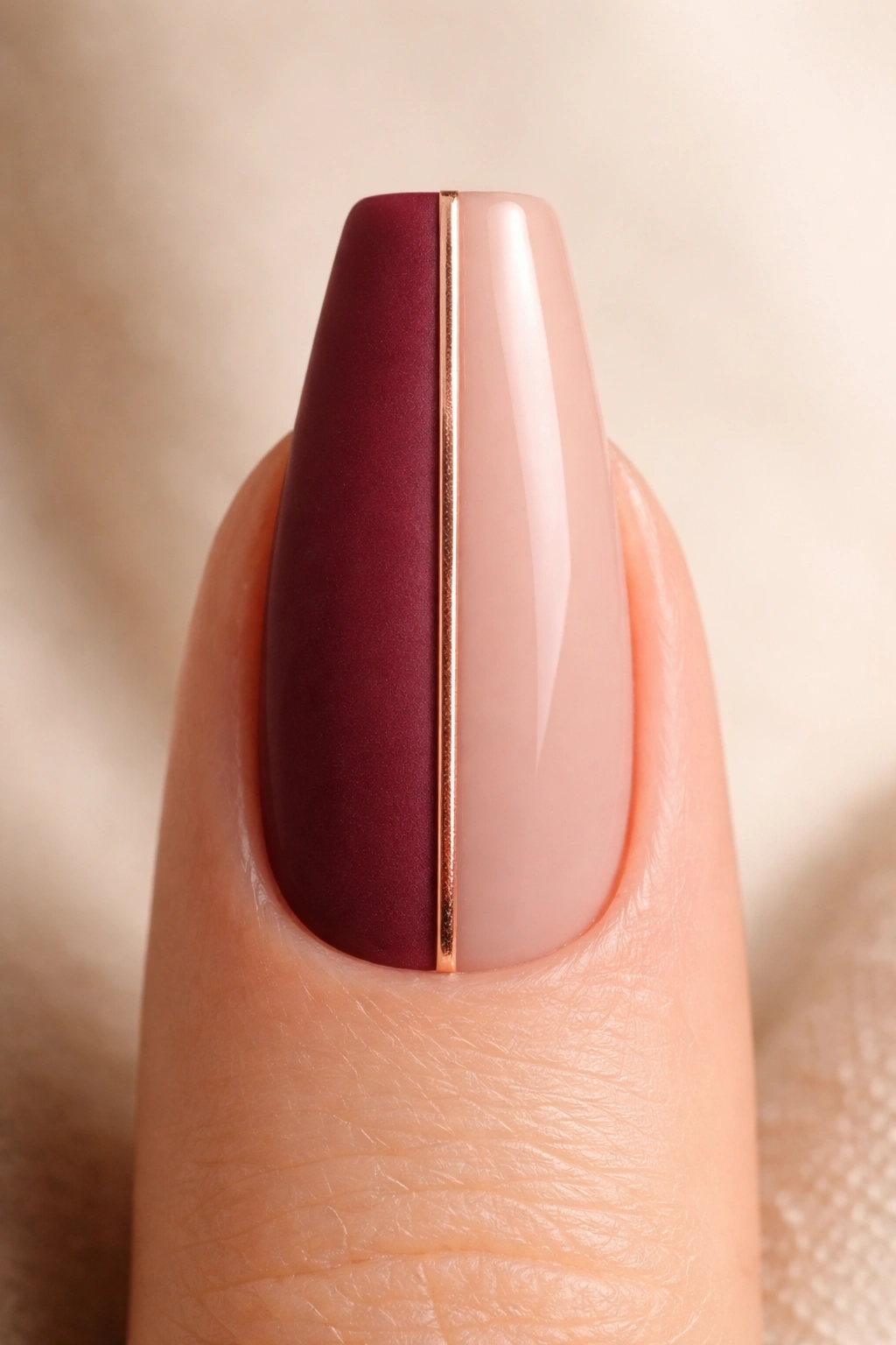 Close-up of a coffin nail with burgundy and nude halves separated by a rose-gold line