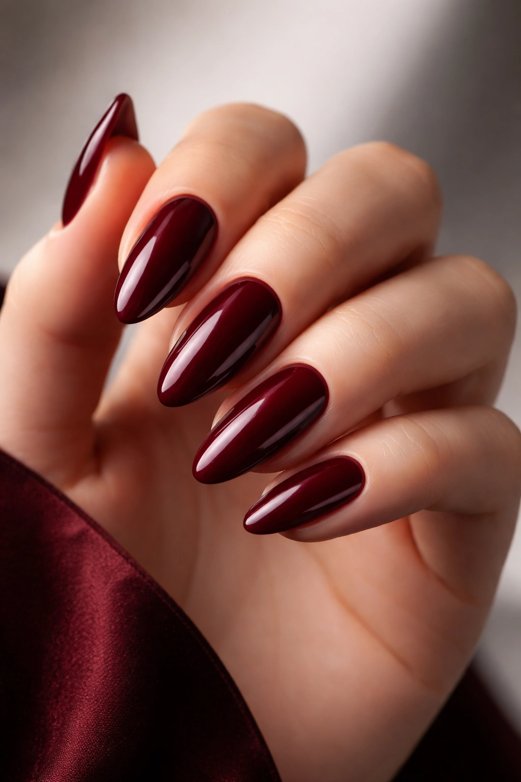 Close-up of a deep vampire red nail with blue undertones and a high-gloss finish on a skin-toned hand