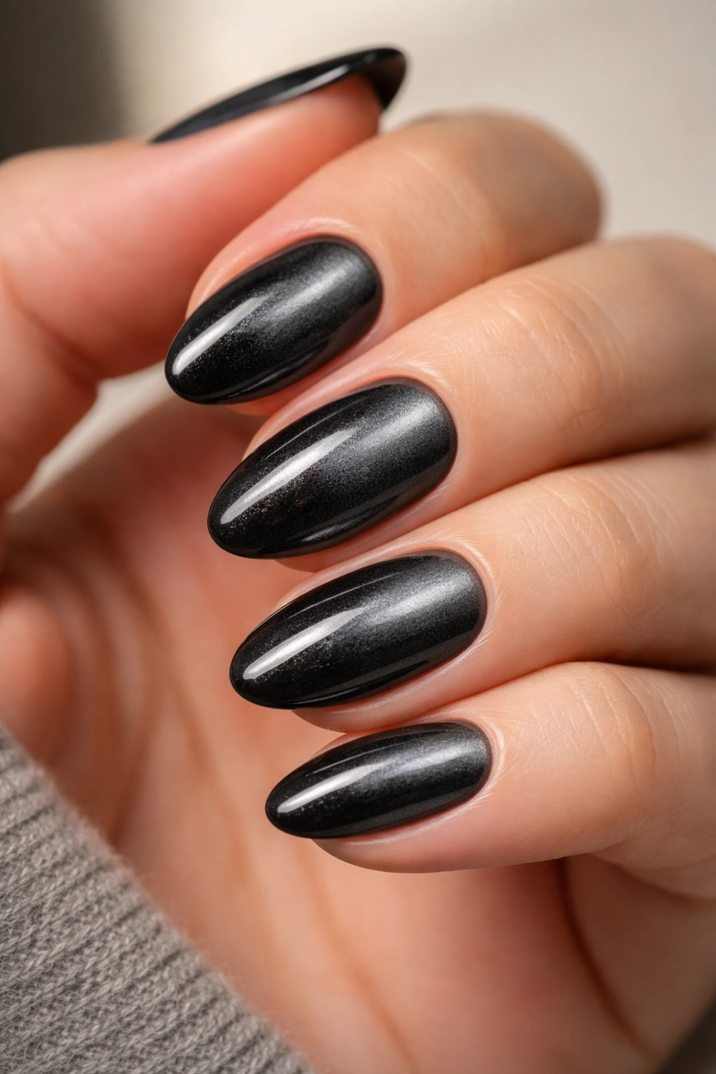 Close-up of short almond nails with velvet black chrome finish that shifts with light