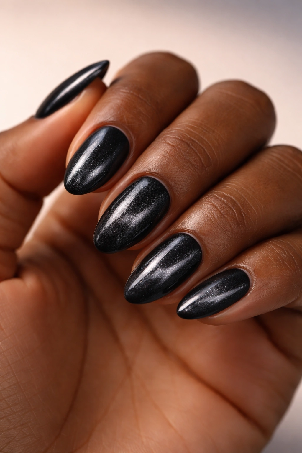 Close-up of velvet black almond nails with magnetic shimmer on dark skin