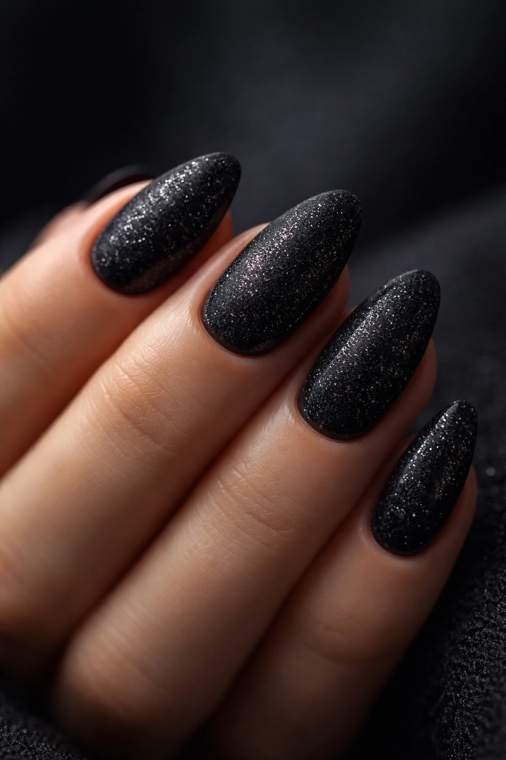 Close-up of short almond nails with deep black velvet glitter finish.