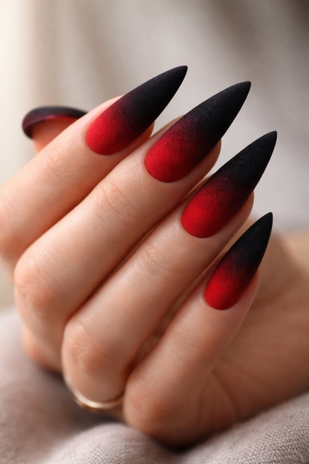 Close up of velvet-textured black-to-red ombre stiletto nails