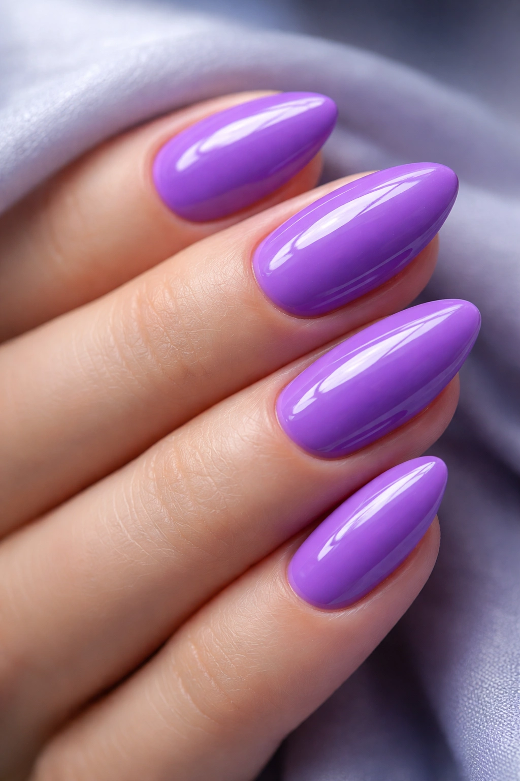 Close-up of short almond nails painted violet purple with a glossy finish