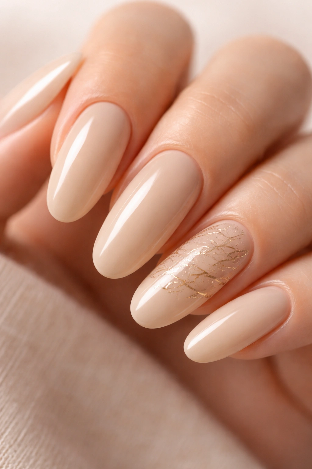Close-up of long round nails with warm beige base and delicate script-like gold accents