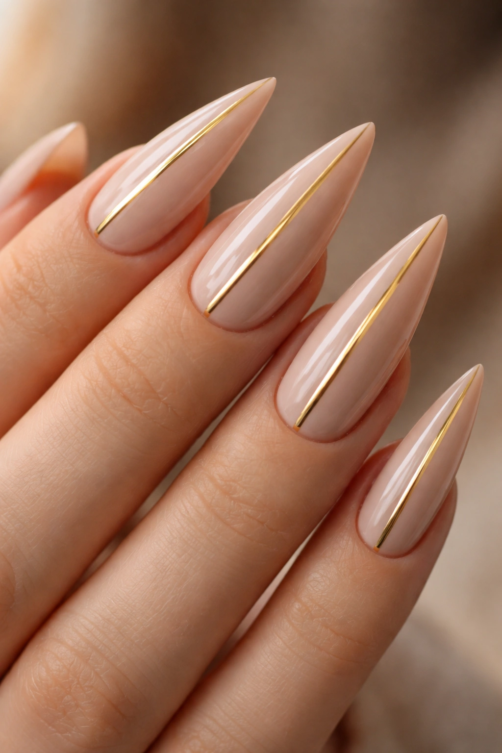 Warm beige stiletto nails with a single gold stripe