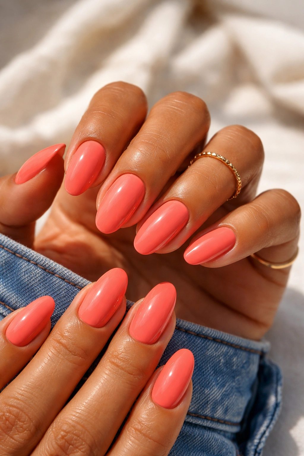 Close-up of warm coral nails on medium skin with glossy finish