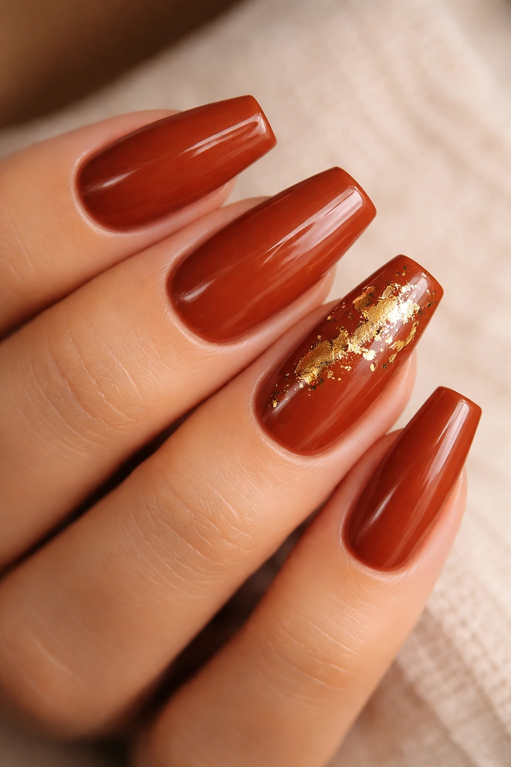 Close-up nails with warm rust and gold foil accent on coffin nails