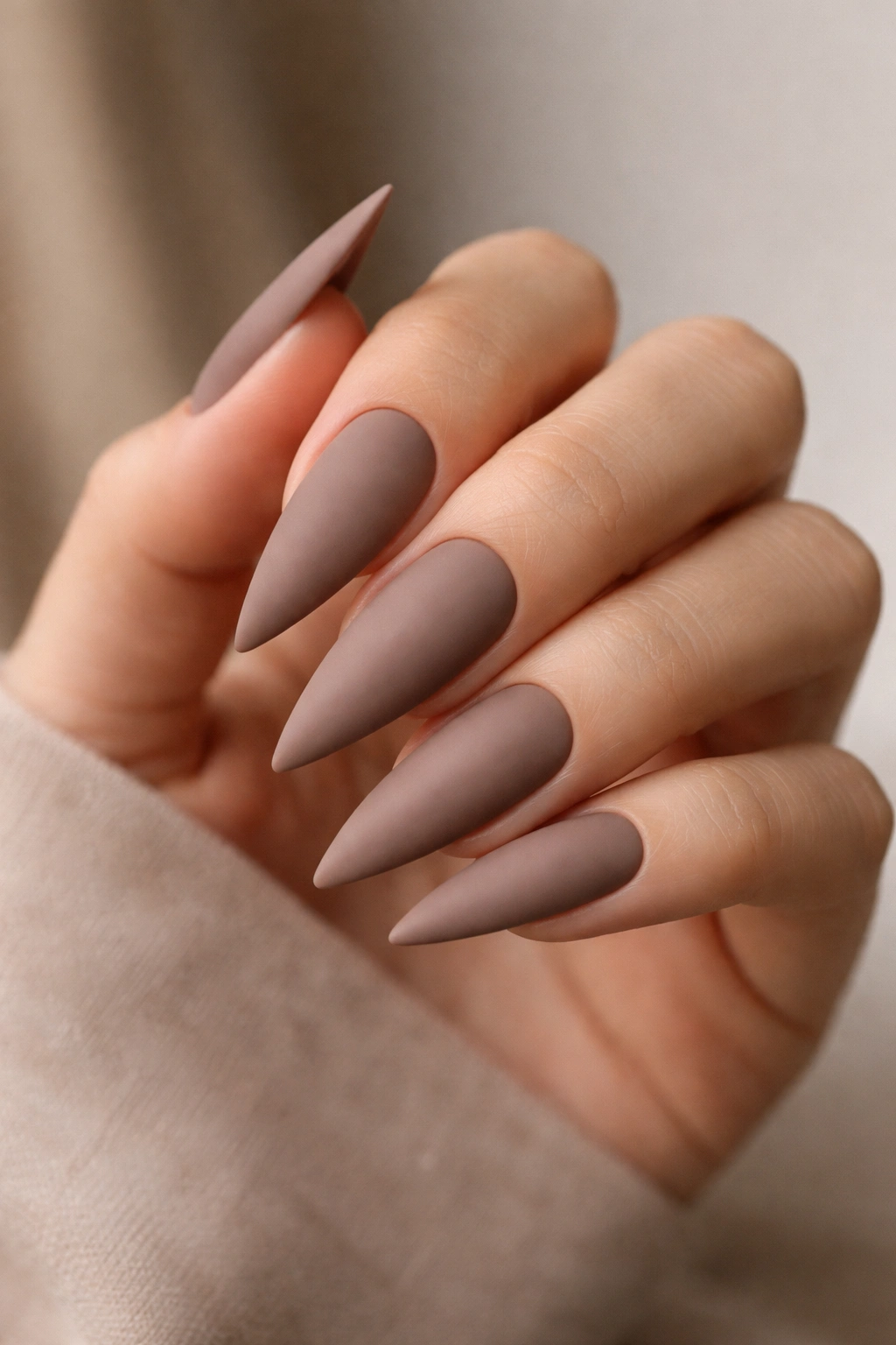 Matte warm taupe stiletto nails on a neutral background