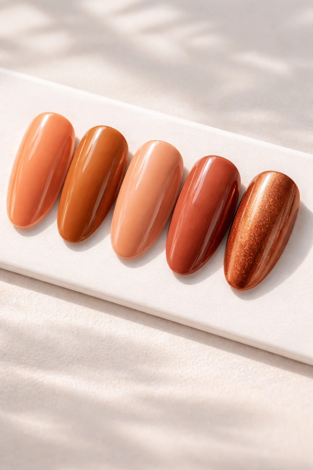 Warm-toned nail polish swatches in peach, caramel, terracotta, nude, and copper under natural light