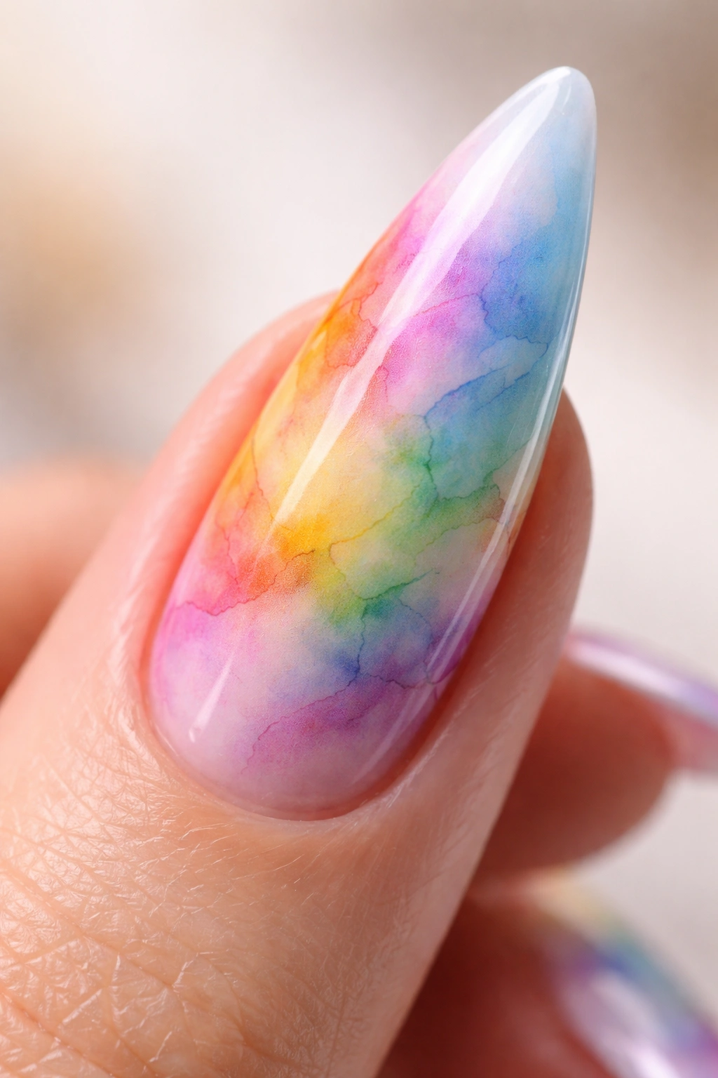 Stiletto nail with watercolor rainbow blend and soft color bleed on neutral background
