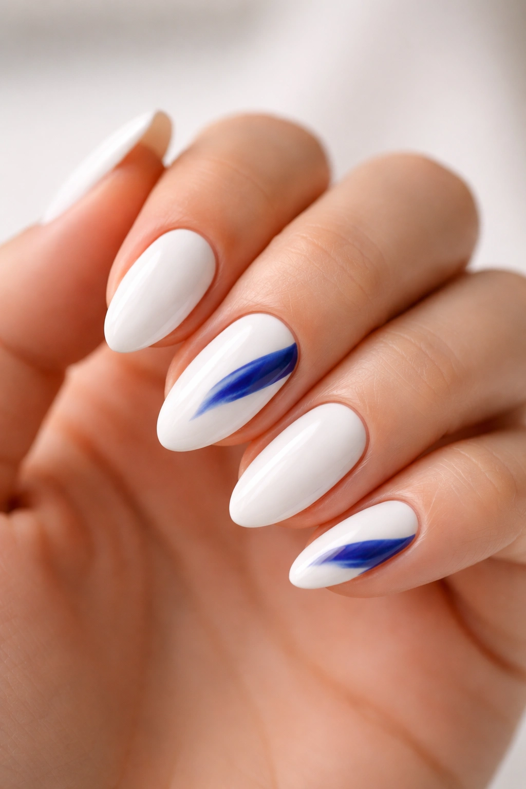 Close-up of white almond nails with cobalt blue abstract strokes