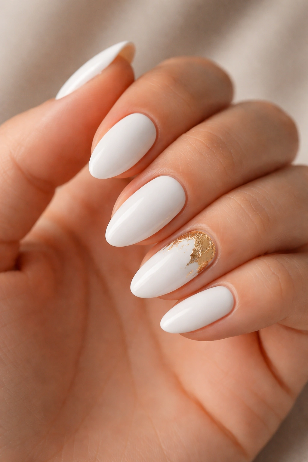 Close-up of white almond nails with a gold foil accent nail on a neutral background