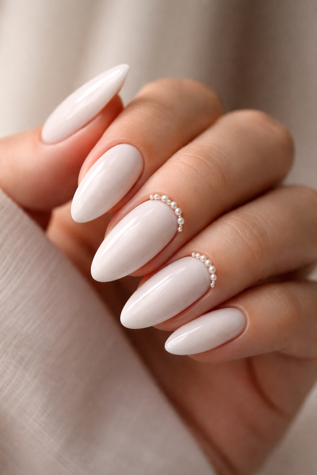 Close-up of white almond nails with tiny pearls along the cuticle