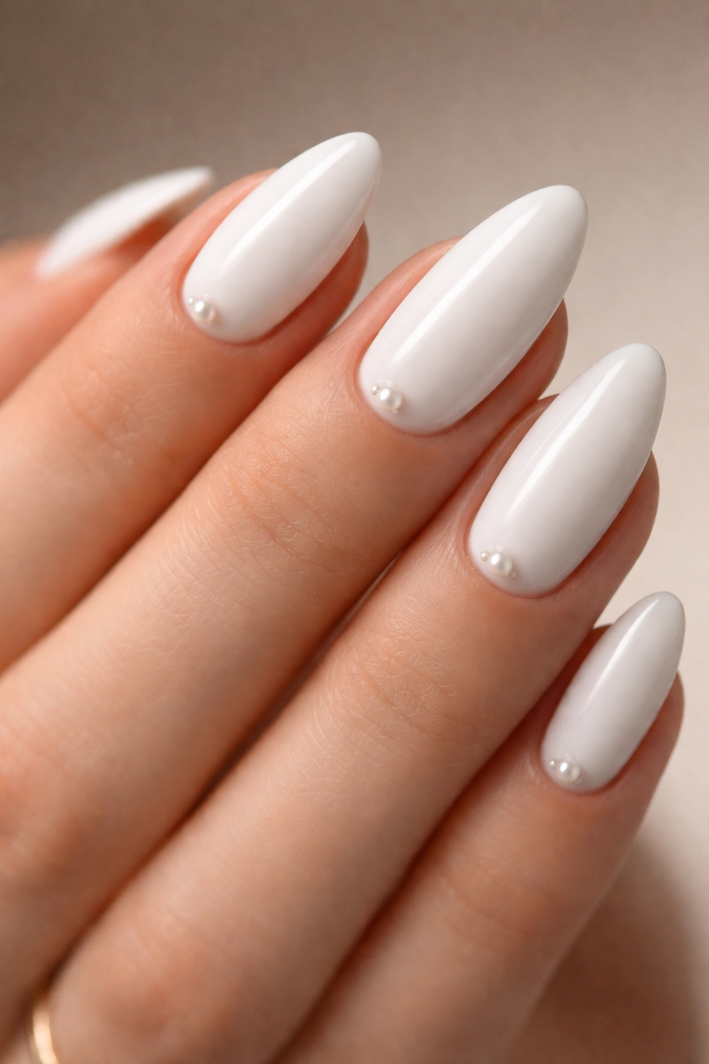 Close-up of white almond nails with tiny pearl accents near the cuticle.
