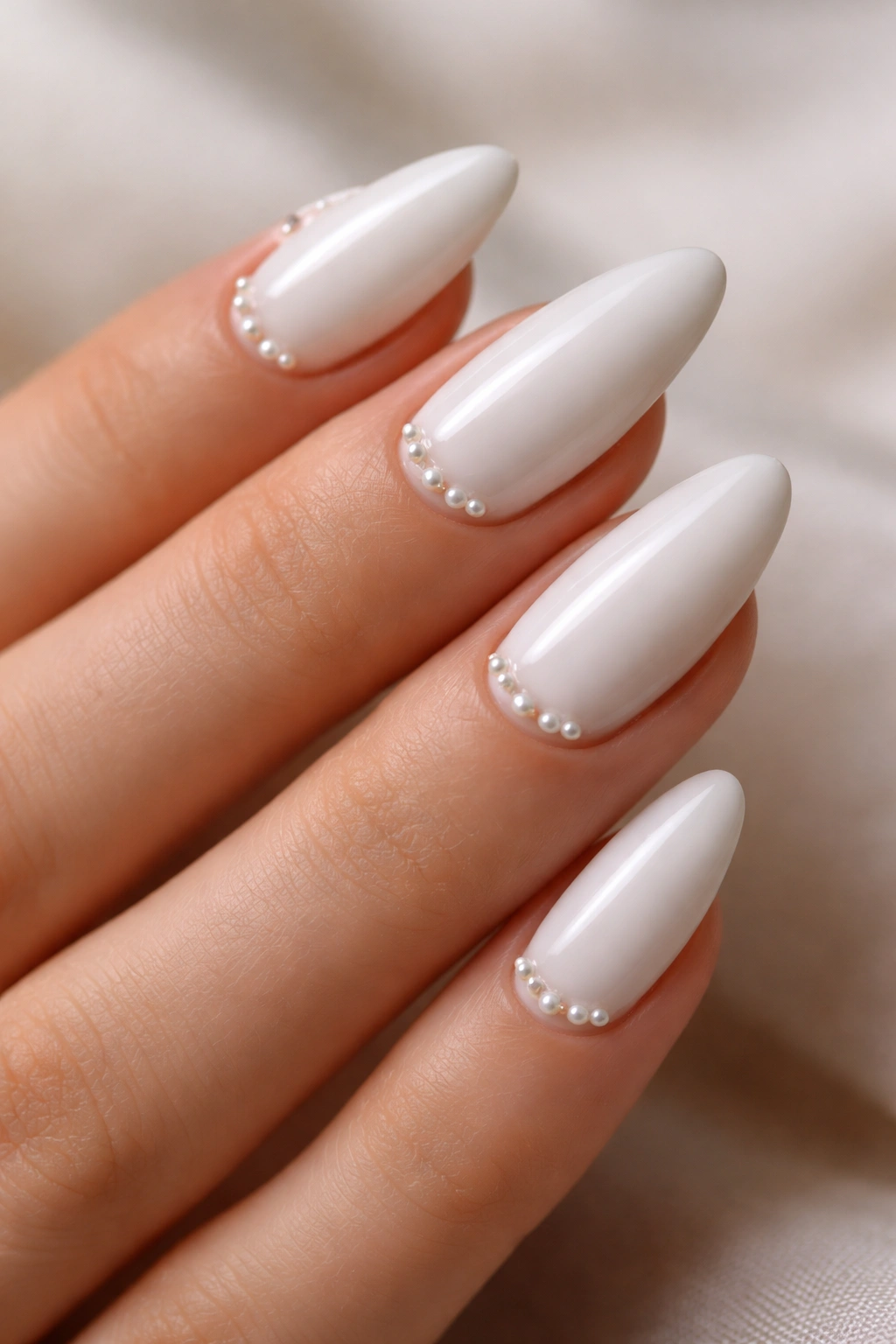 Close-up of almond-shaped white nails with tiny pearl accents near the cuticle
