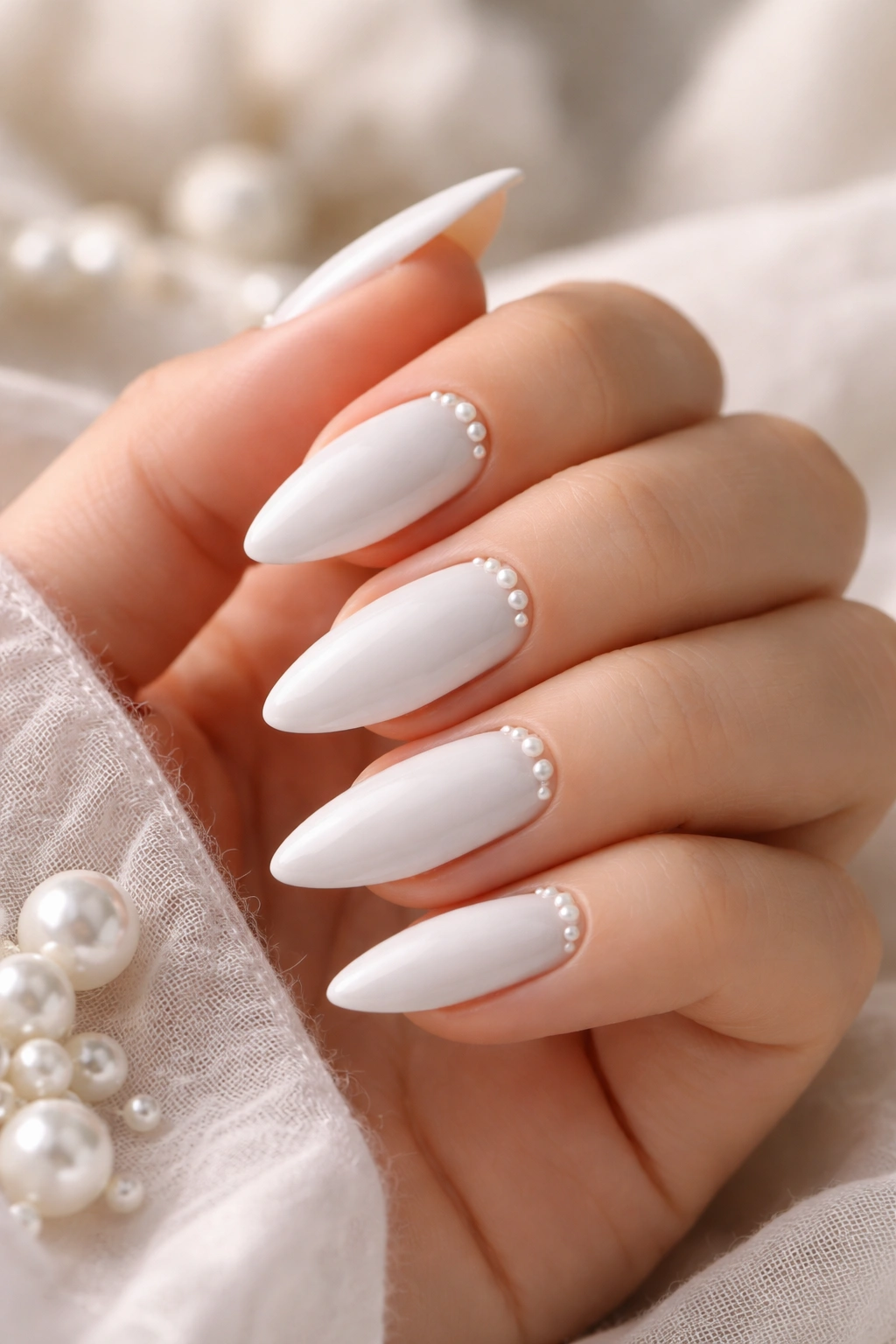 Close-up of white almond nails with tiny pearls near the cuticle on a glossy finish