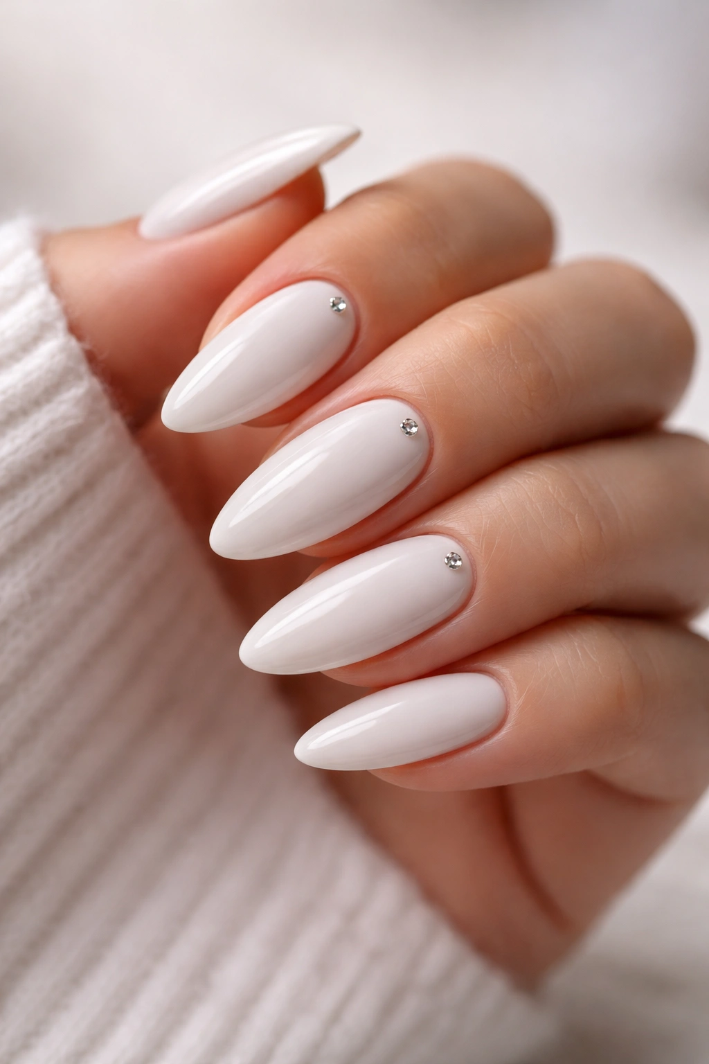 Close-up of white almond nails with tiny rhinestones near the cuticle.