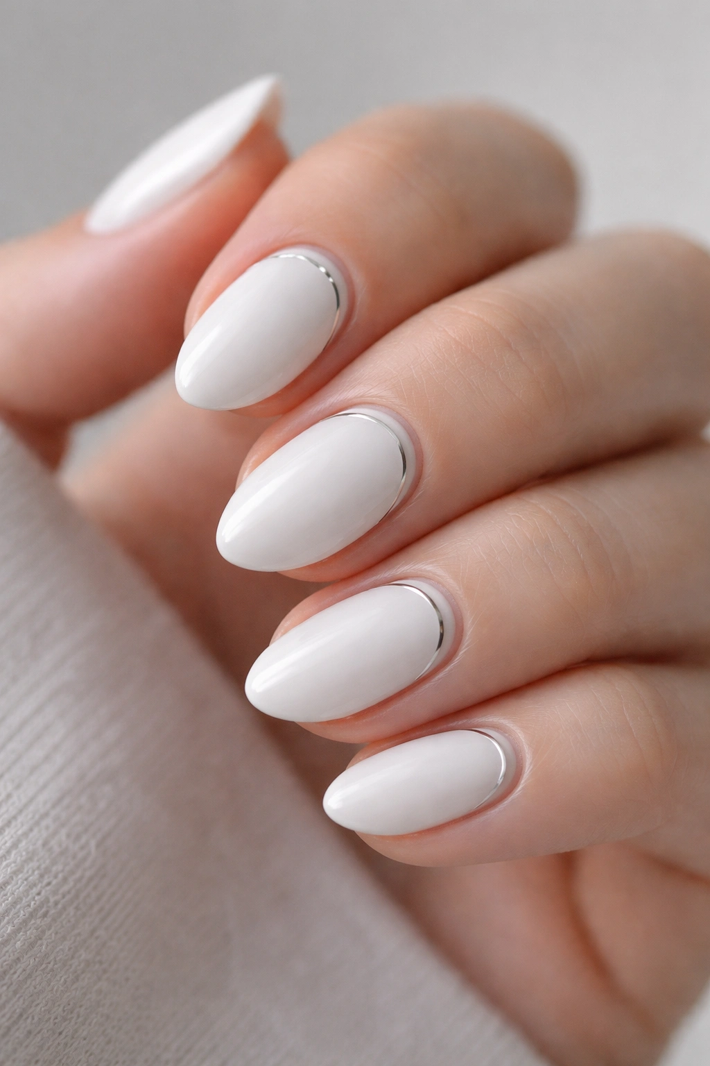 Close-up of white almond nails with silver chrome lines on a pale hand