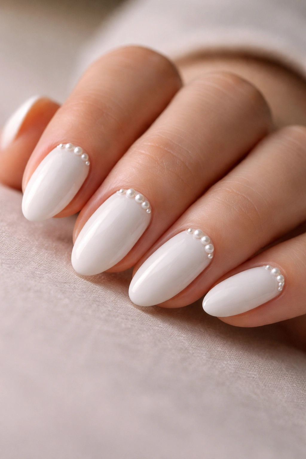Close-up of short white almond nails with tiny pearl accents near the cuticle