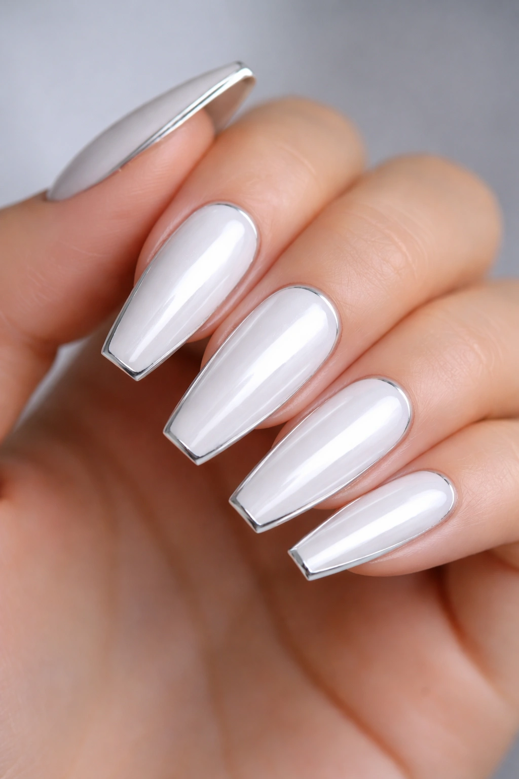 Close-up of snow-white chrome ballerina nails framed by a thin silver outline