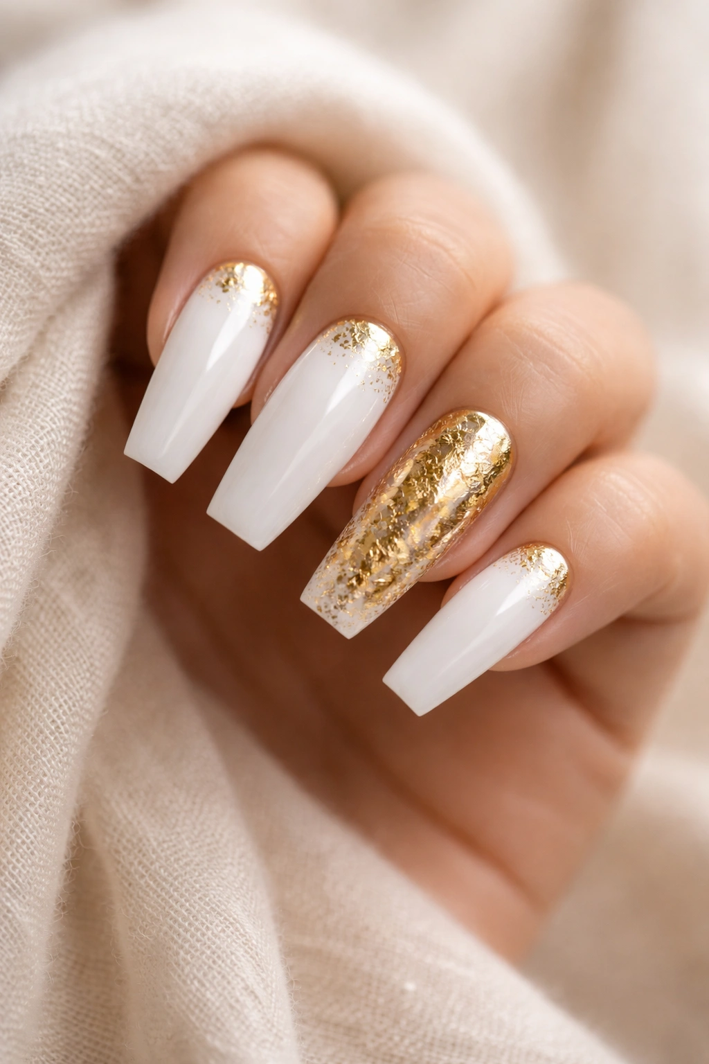 Close-up of white coffin nails with gold foil accents on a hand