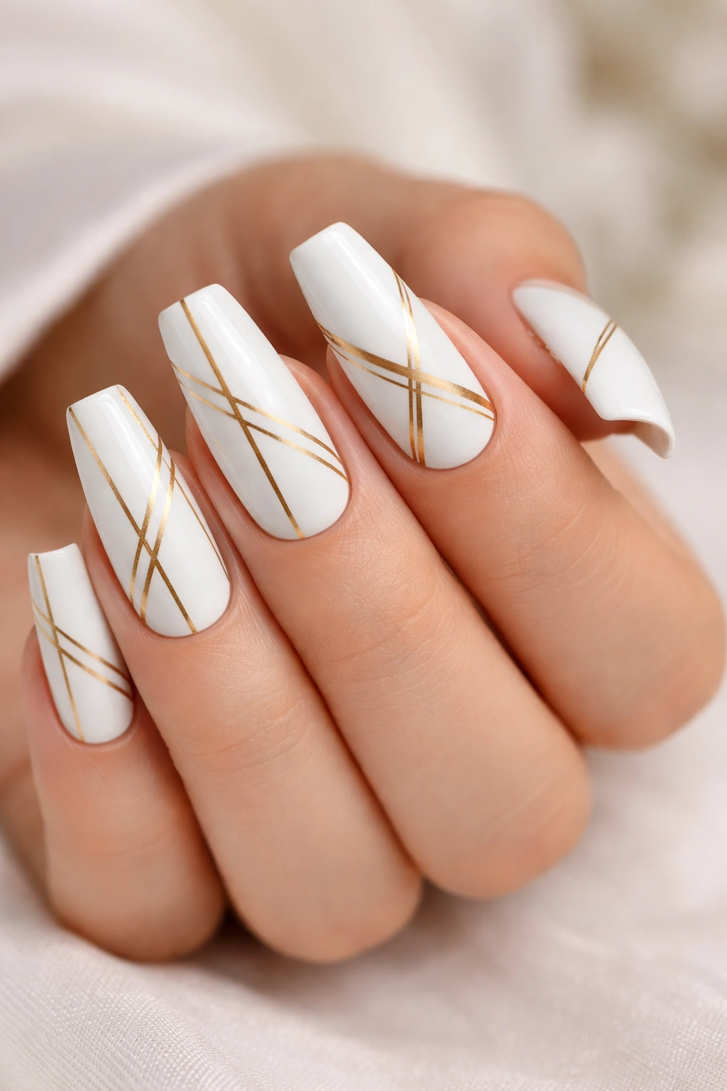 Close-up of white coffin nails with gold geometric striping for modern wedding manicure