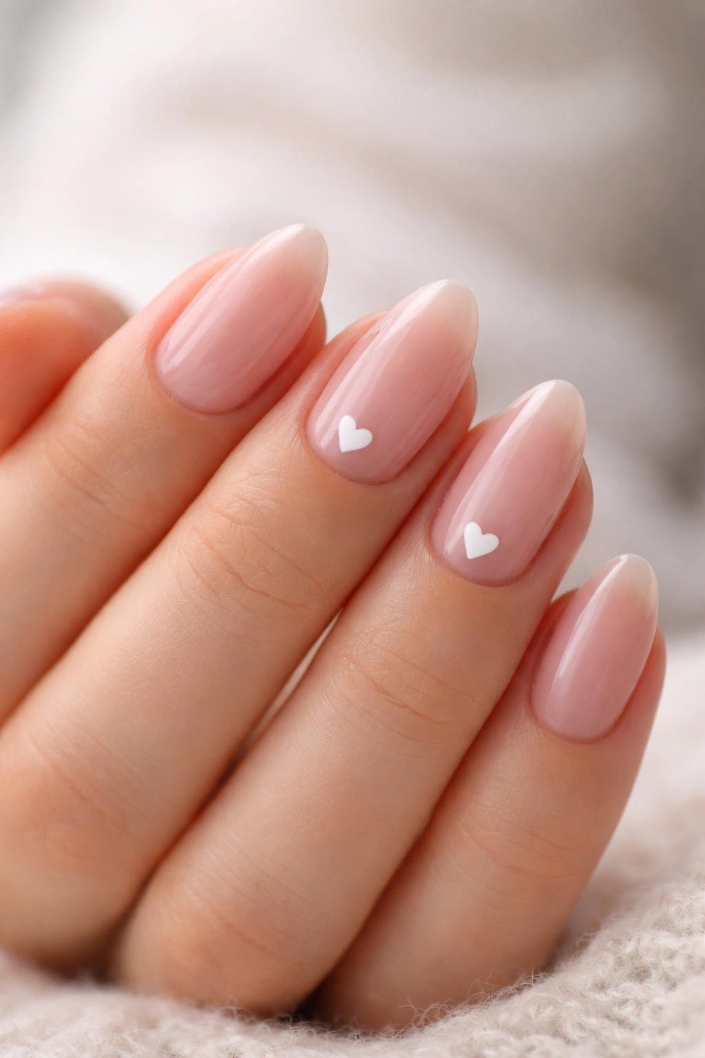 Close-up of short almond nails painted rosy pink with small white hearts on accent nails