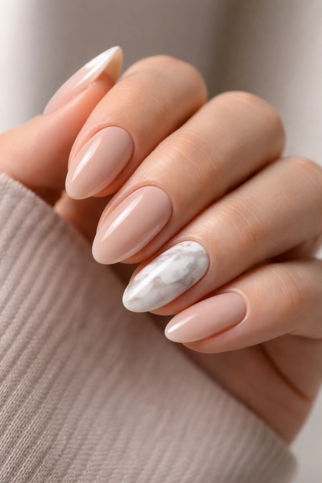 Close-up of nude-based nails with white marble accents on short almond nails