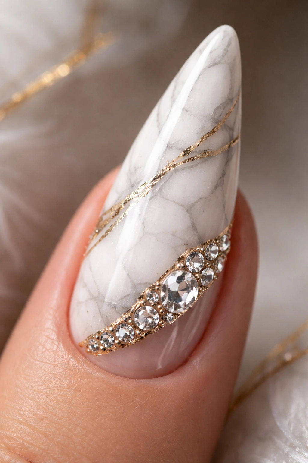 Close-up of a white marble-styled stiletto nail with gold accents and rhinestones
