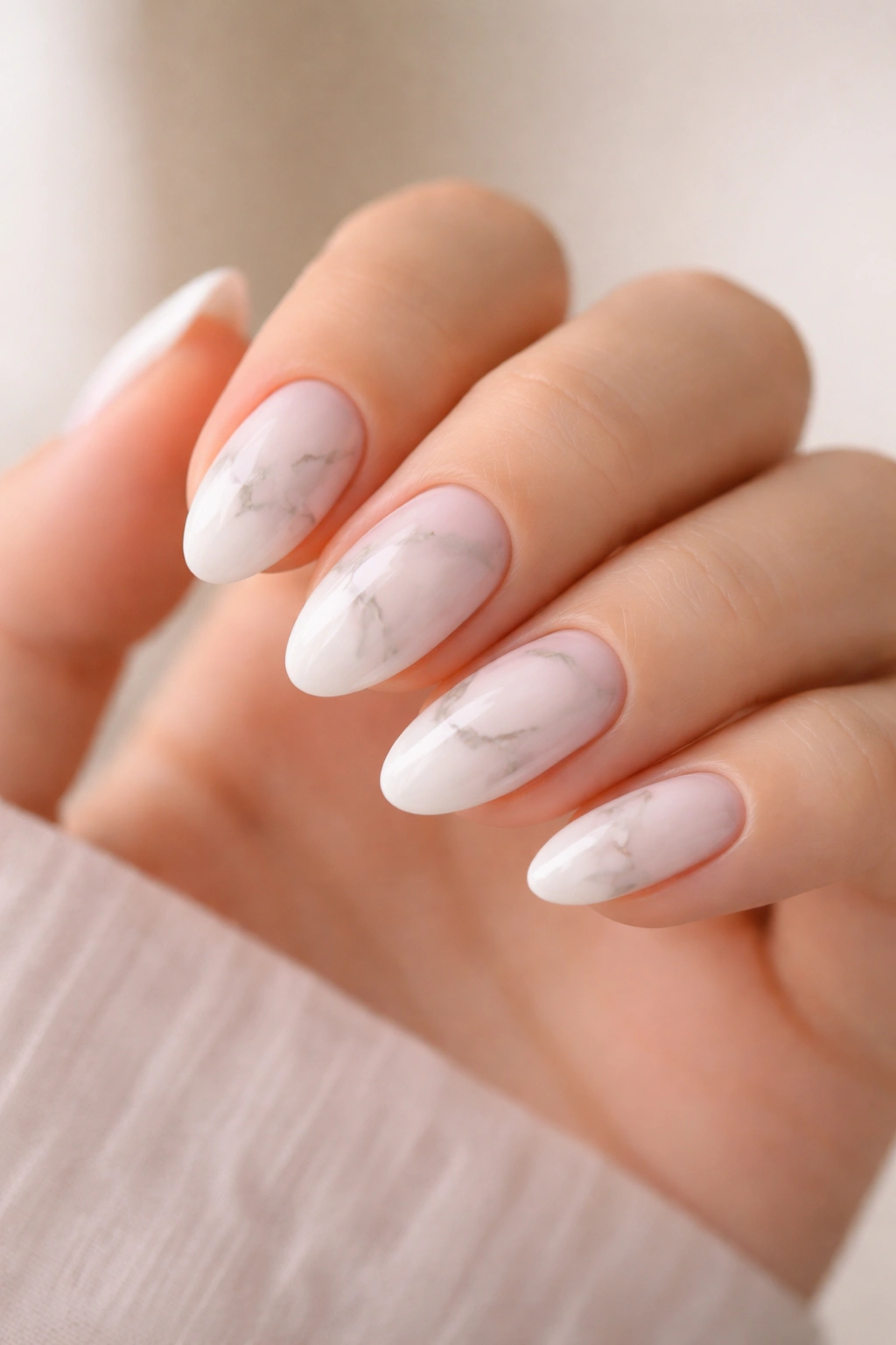 Close-up of short almond nails with white marble and gray veining on sheer pink base