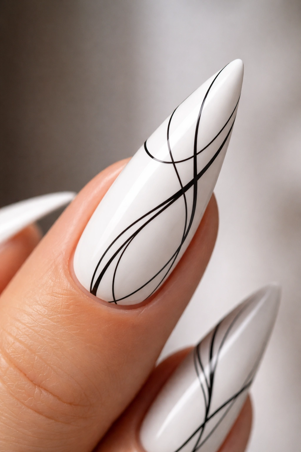 Close-up of white nail with black line art accents on a stiletto shape