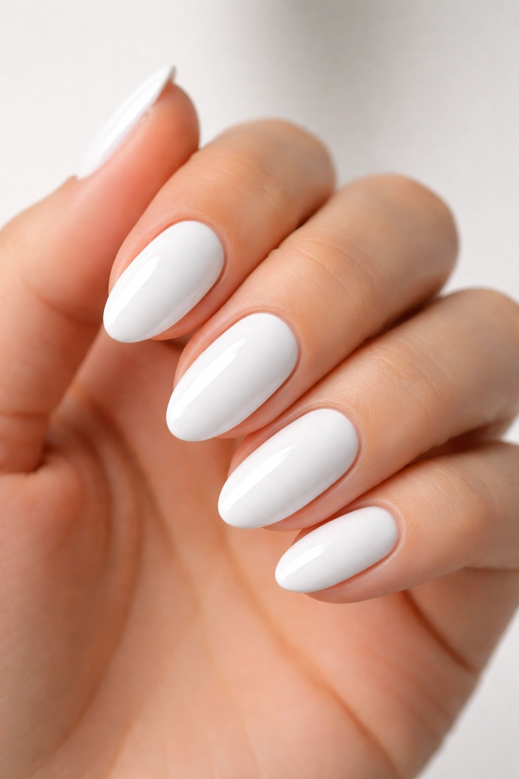 Close-up of short almond nails in glossy white with sharp edges.