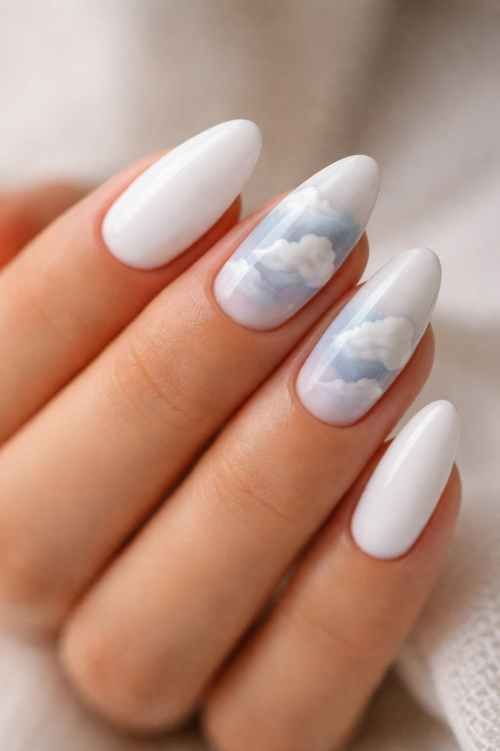 Close-up of white almond nails with soft cloud art on accent nails