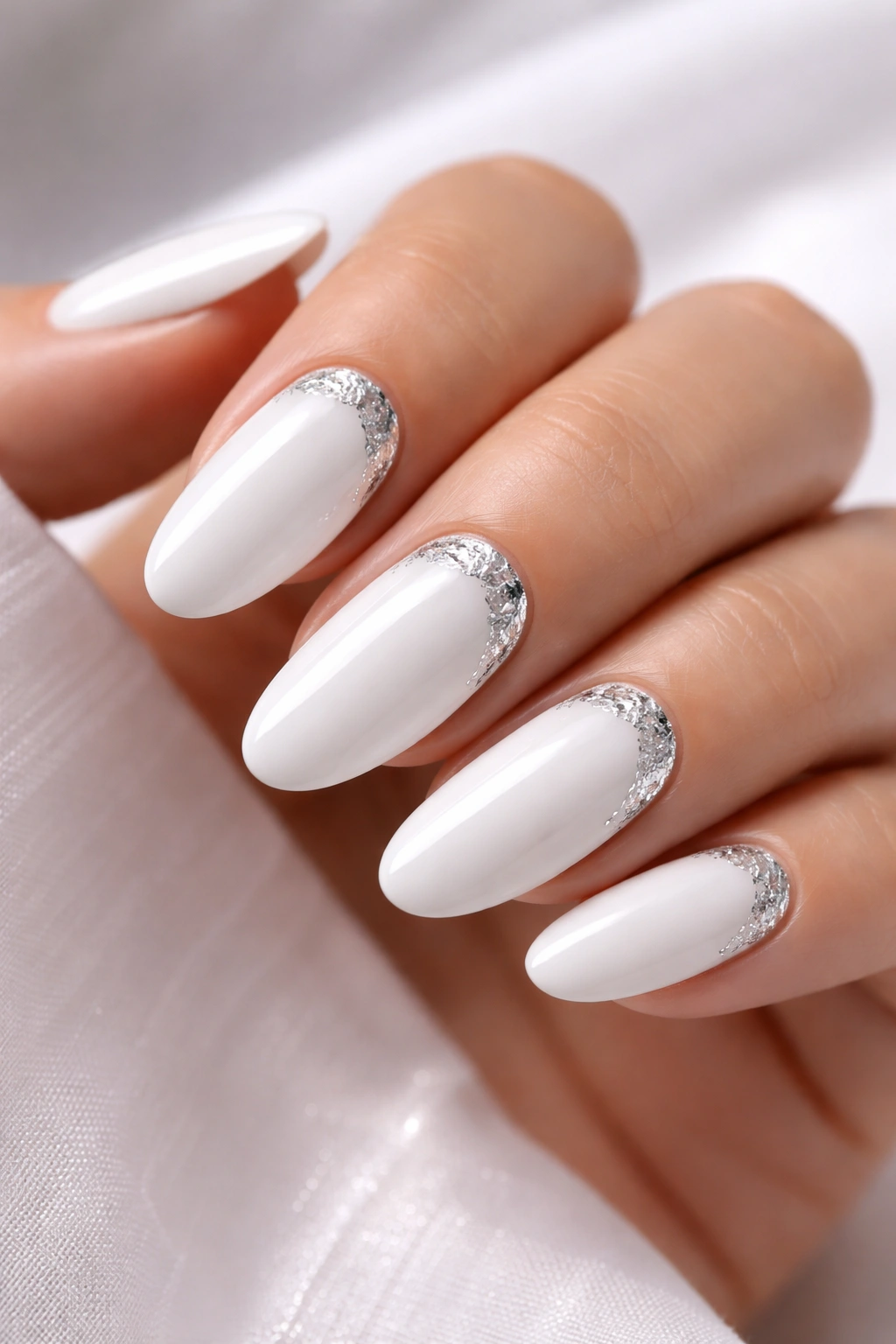 Close-up of white long oval nails with silver foil accents