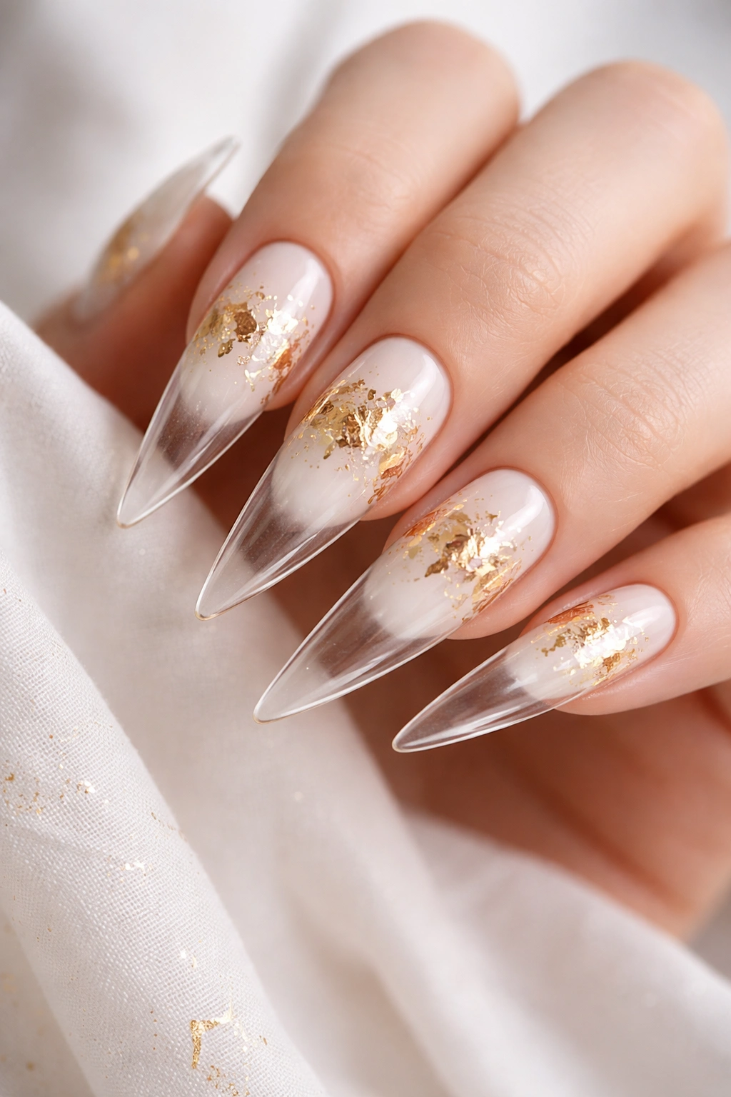 Close-up of white nails with gold leaf accents and clear gradient tips