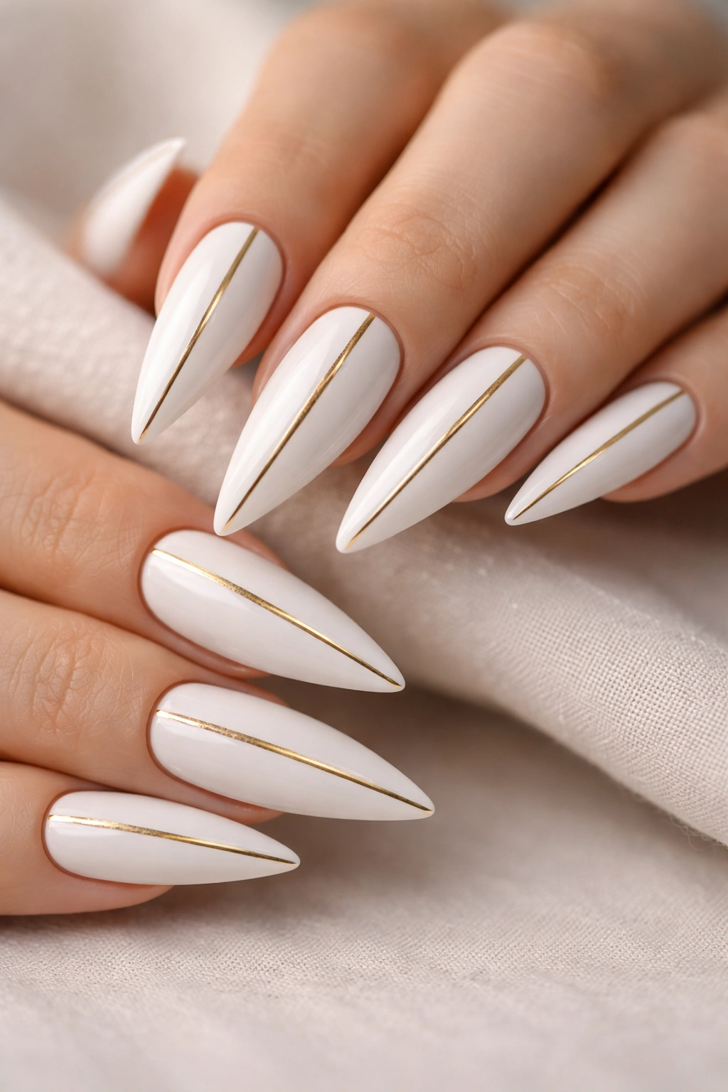 Close-up of white stiletto nails with a single vertical gold stripe on each nail