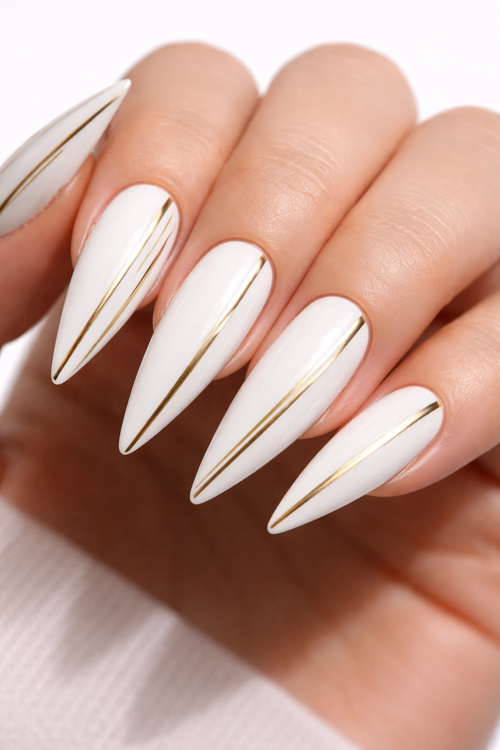 Close-up of white stiletto nails with gold stripes on a white studio background
